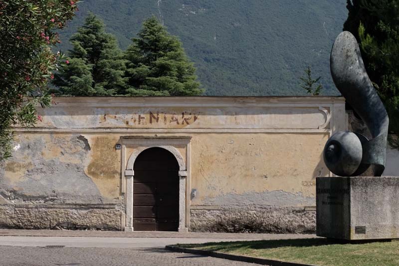 A short tan building with a rounded entrance in front of a steep wooded mountain