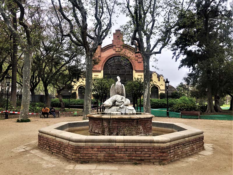 fountain surrounded by park benches, building in background