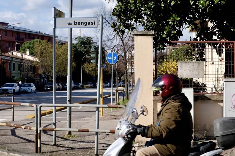 A person wearing a coat and helmet riding a moped on a street corner