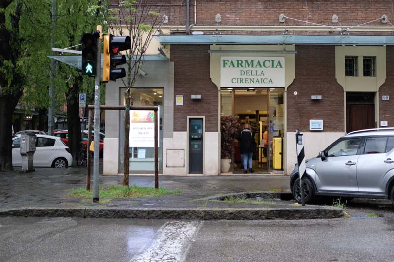 A pharmacy on a street corner with a car parked in front of it