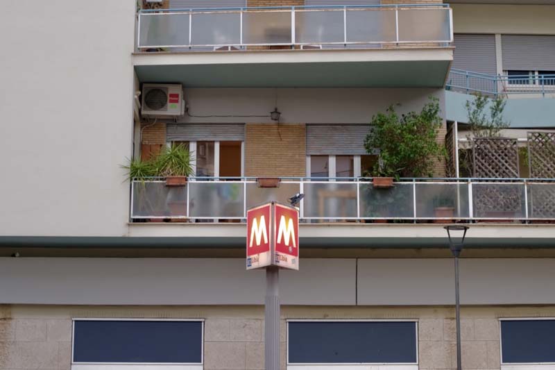 A metro sign in front of a building with a balcony and plants