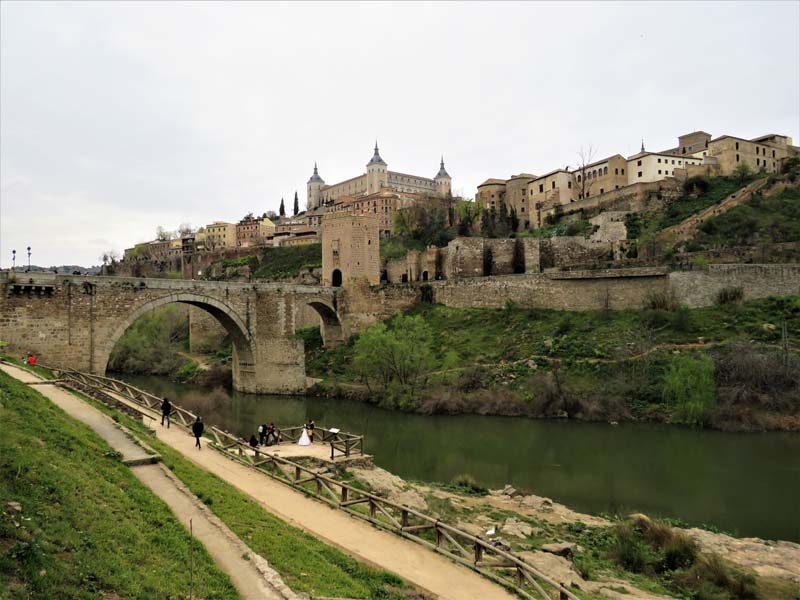 view of river with stone bridge and city in background