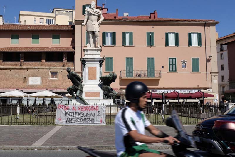 A person riding a moped in the foreground with a building and statues in the background