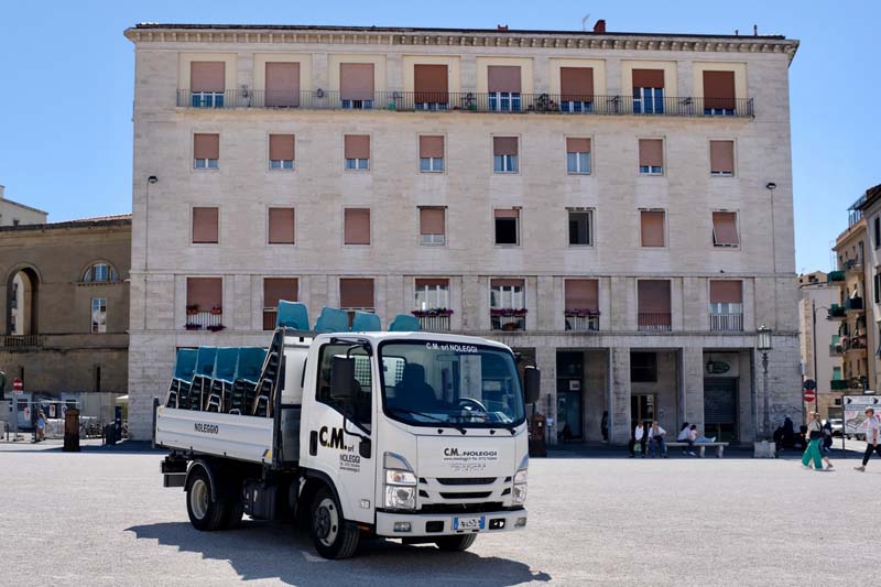 A truck carrying chairs sits in front of a multi-story building