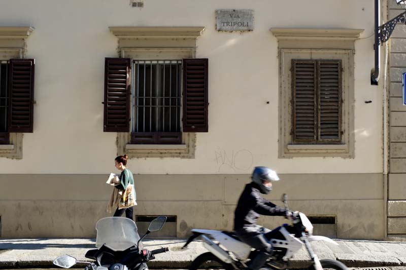 A person walking and a person riding a motorcycle next to a building with windows and shutters