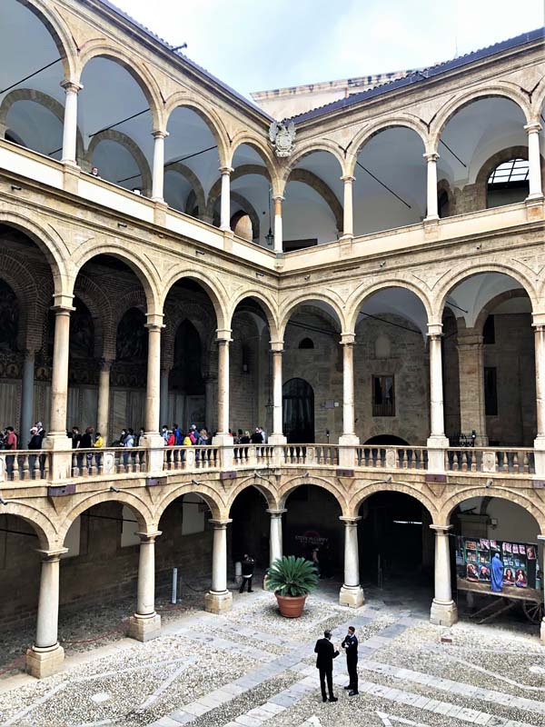 courtyard surrounded by three-story colonnade. people line up on second story.