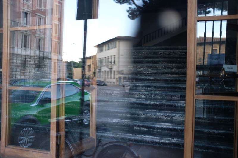 A window reflection showing a green car and buildings