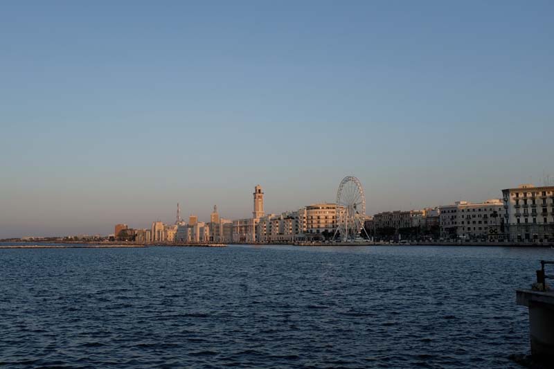 Several buildings and a Ferris wheel line the waterfront against a blue and purple sky