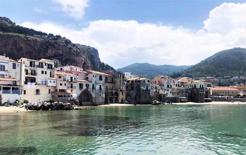 view from water of buildings lining coast with mountains in background