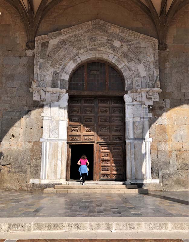 woman walk through arched stone doorway with wooden doors