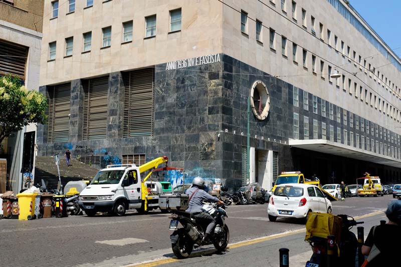A building corner with several work trucks parked in front and cars driving by on a street