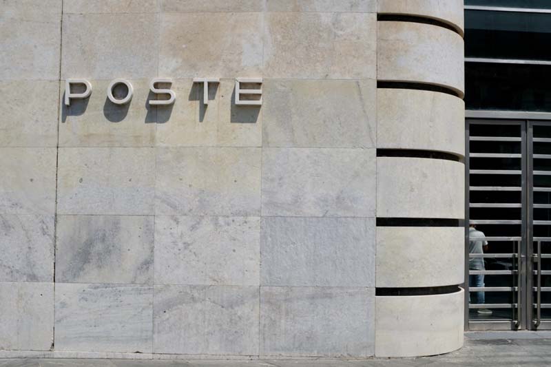 The exterior of a building with a smooth, light gray wall and large letters mounted on the building