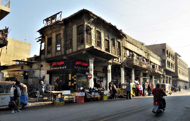 crumbling row of retail buildings with goods on sidewalk along street