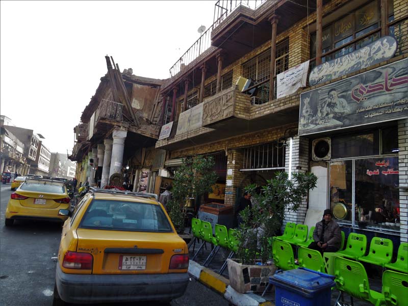 two yellow cars in street alongside deteriorating building storefronts