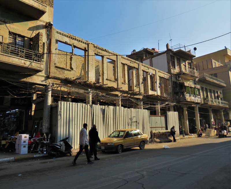 facade of concrete and brick buildings with boarded up, roofless building in center