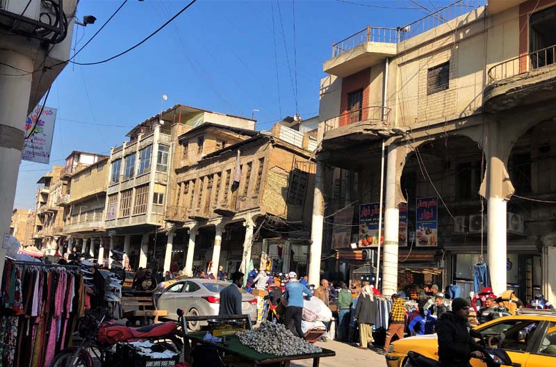 crowded street scene with vendors, buildings with colonnade, crumbling facades