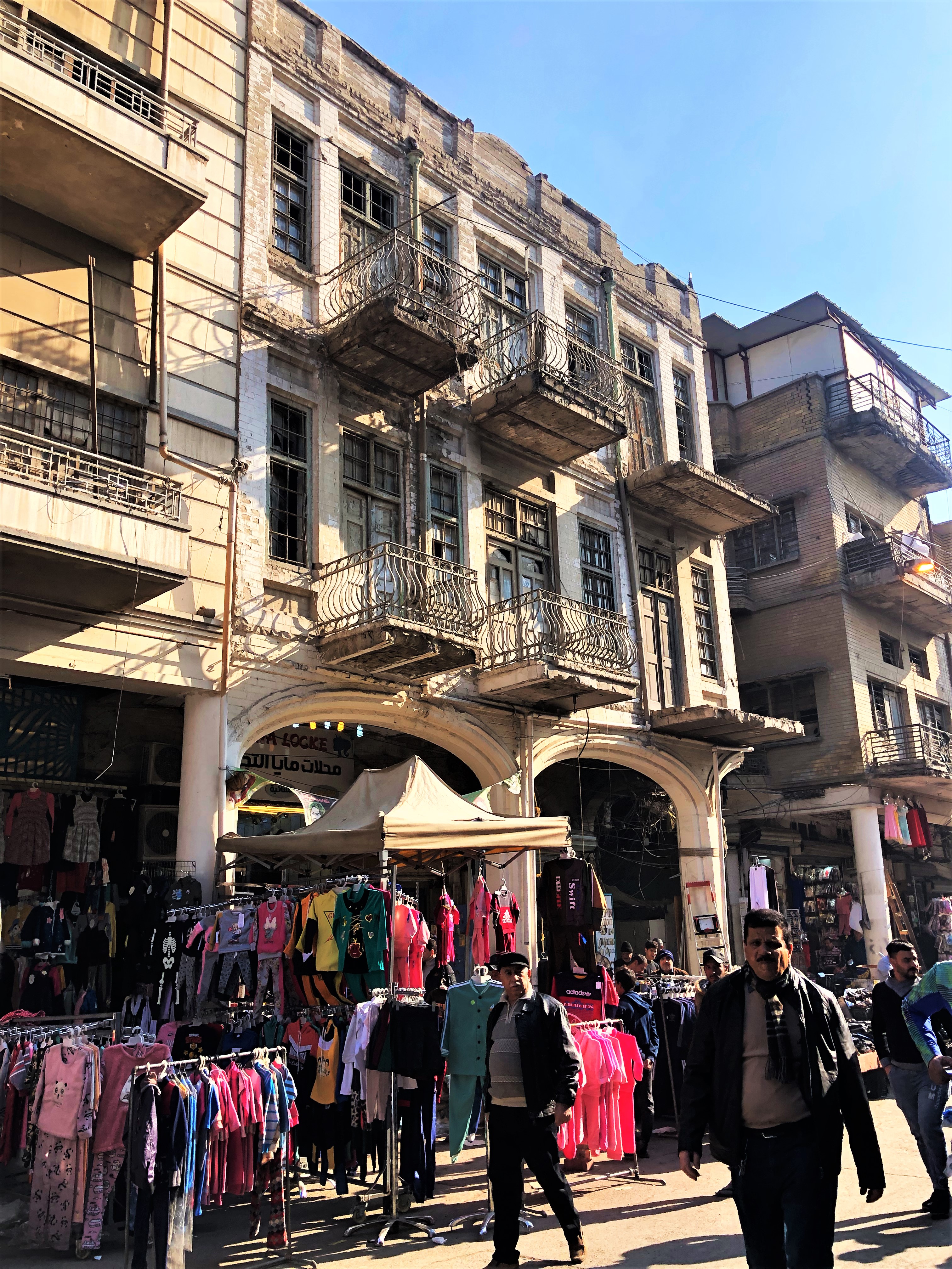people walk down street filled with racks of clothes alongside three-story facade