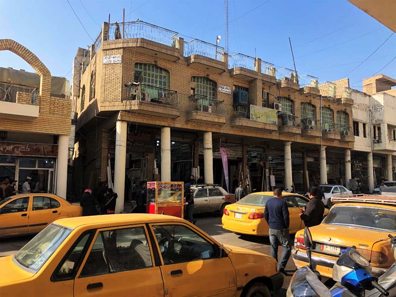 yellow cars in foreground, crumbling yellow-brick colonnade building in background