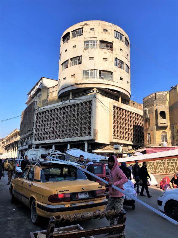 concrete building withe cylindrical top and square base, street scene in foreground