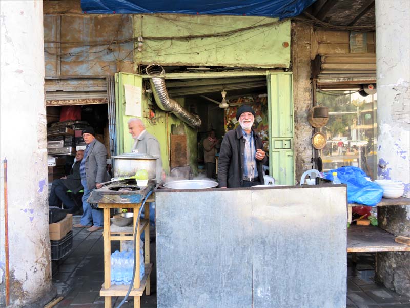 man with gray beard smiles at camera among street vendors