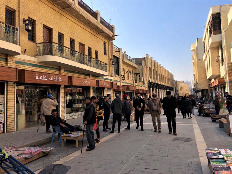 people walking on paved road with retail shops on either side