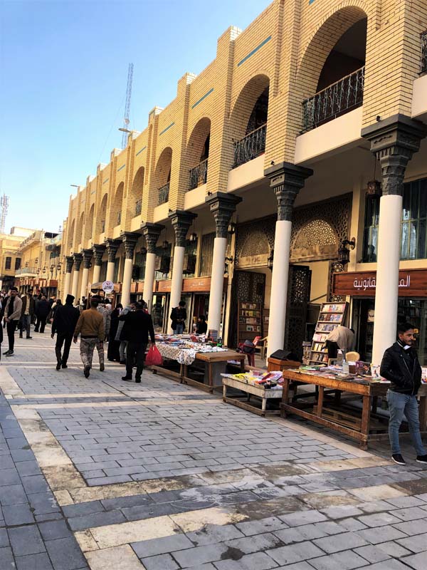 people walk down paved walkway with yellow brick colonnade storefronts