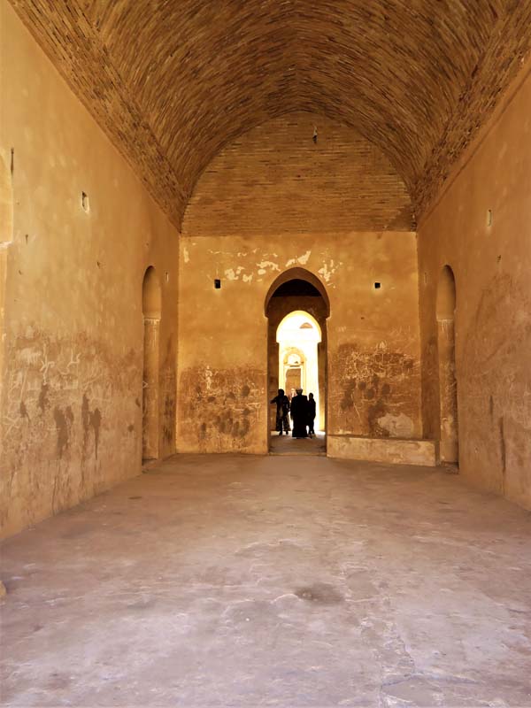 people stand in corridor beyond doorway of barrel-vaulted room