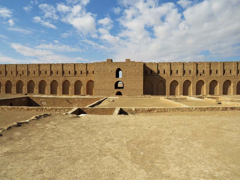 tops of buildings in foreground, arched fortress wall in background