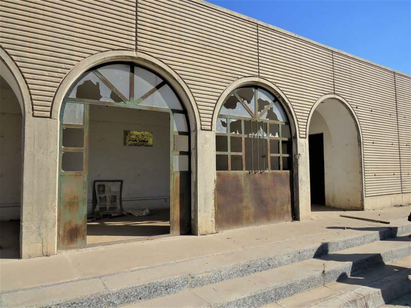 concrete facade with arched doorways with broken glass
