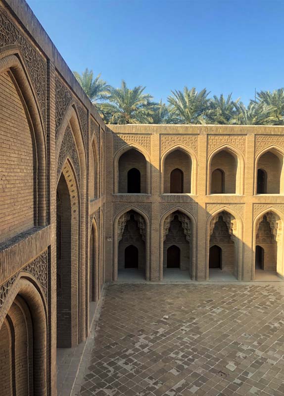 view into courtyard, palm tree rise above double arcade