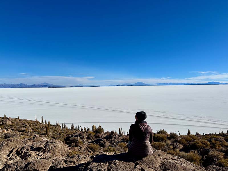 person sits on rock looking onto vast salt flat