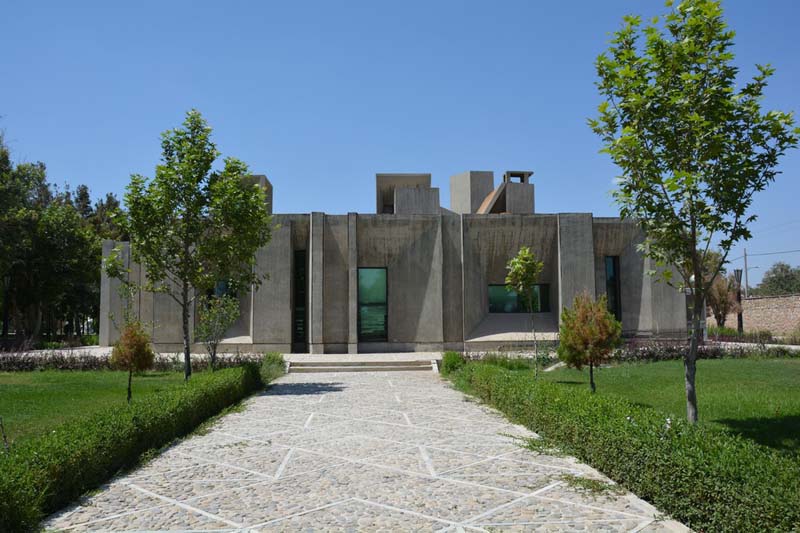 A straight stone walkway leads through a grassy lawn to a low concrete building
