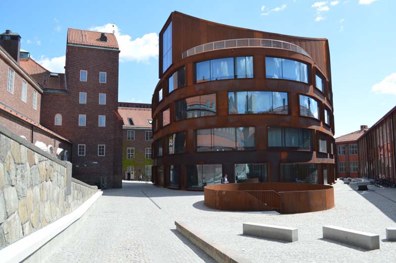 A rust-colored building with courses of large windows in a curving facade