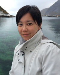 Vimalin Rujivacharakul, a woman with dark hair, wears her hair pulled back, a white jacket, with a water and cliffs in background