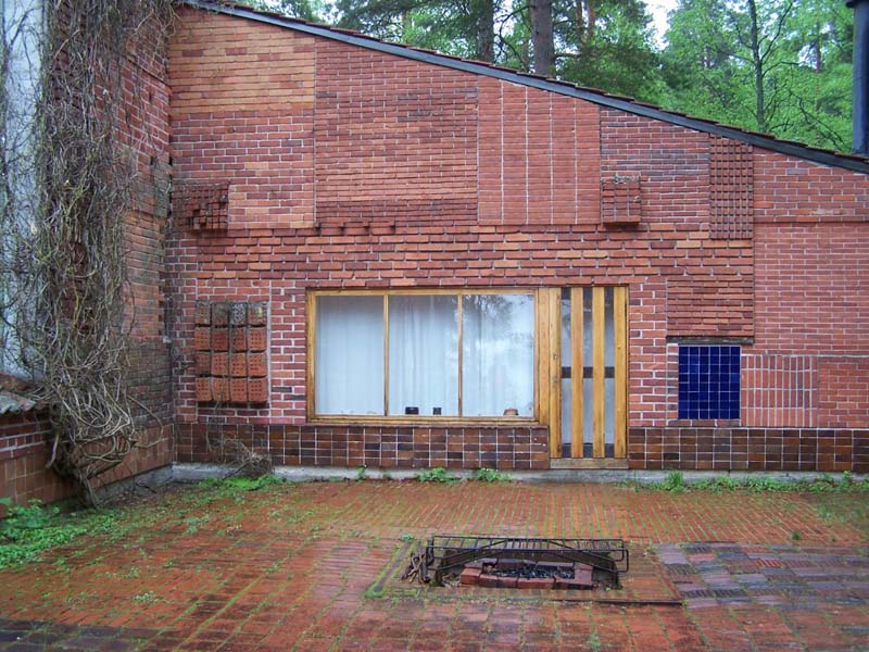 A row of three windows and a door are surrounded by a wall of brickwork displaying a variety of block sizes and patterns.