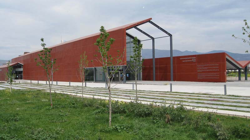 A long, red building stands with one end open to a recessed glass facade