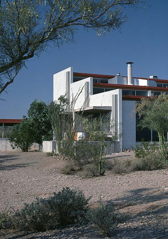white, gray, and brown house with tripartite stepped form, tall glass windows, set in desert landscape