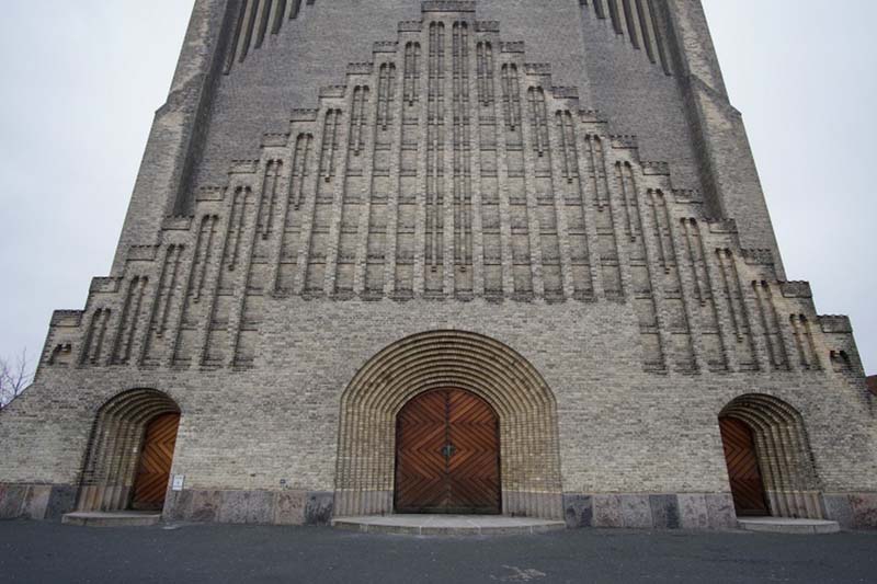 Doors with geometric patterns are framed by receding concentric arches below a stepped triangular projection with neogothic embellishments