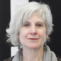 Ann Whiteside, a white woman with short gray hair, wears dangle earrings, gray scarf, and dark gray jacket