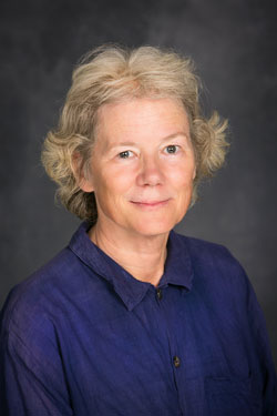 woman with blond hair wearing blue button-down shirt against a gray background