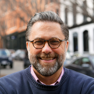 Man with brown glasses, blue sweater, and grey hair