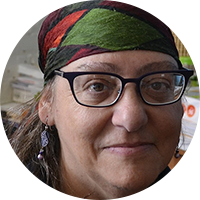 Head shot of a white woman with patterned scarf, glasses, and earrings, and shoulder length hair faces camera. 