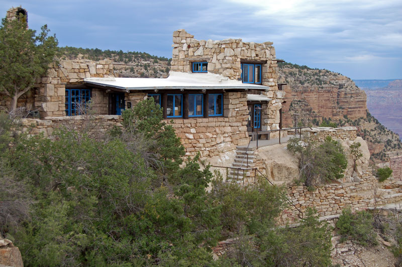 multi-level stone masonry building with blue windows surrounded by canyon cliffs