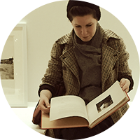 Michal Shumate, a woman with brown hair, wears a brown hat, scarf and coat, looks down and reads a book