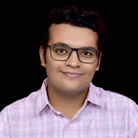 Yakin Kinger, an Indian man with glasses and a pink shirt, smiles at the camera