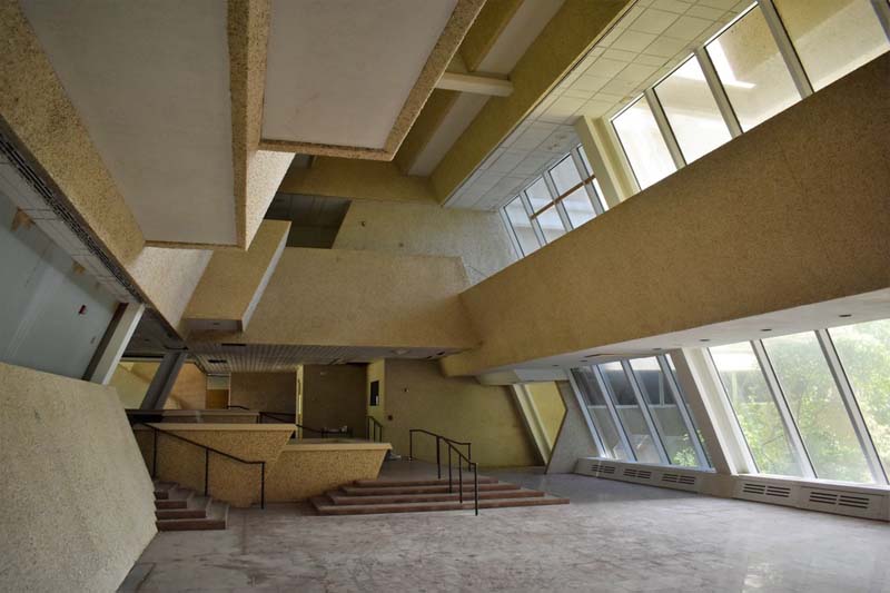 angular concrete interior with multiple levels, low stairways with simple railings, large glass windows