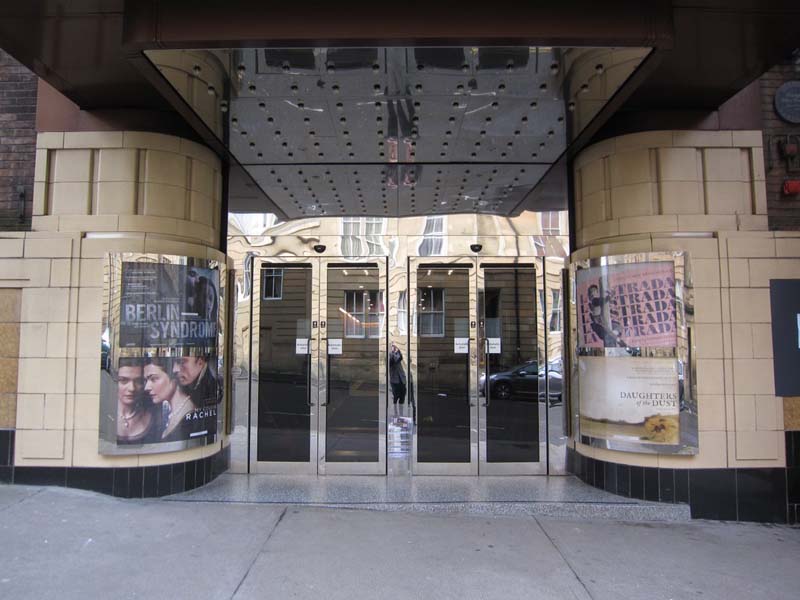 stainless steel and glass double doors flanked by curved walls with movie posters
