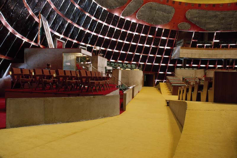 auditorium with red chairs, yellow floors, low concrete walls, and brick red walls