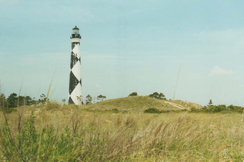 white lighthouse with black diamond pattern with grassy field in foreground