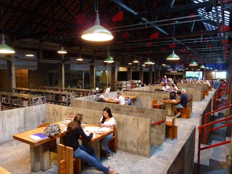 industrial space with people working at tables partitioned off with low concrete walls, bookshelves in rear